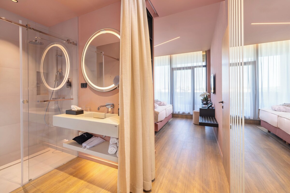 Ein modernes Badezimmer mit Glasdusche, Waschtisch inklusive Spiegel und einem Bett mit Blick.