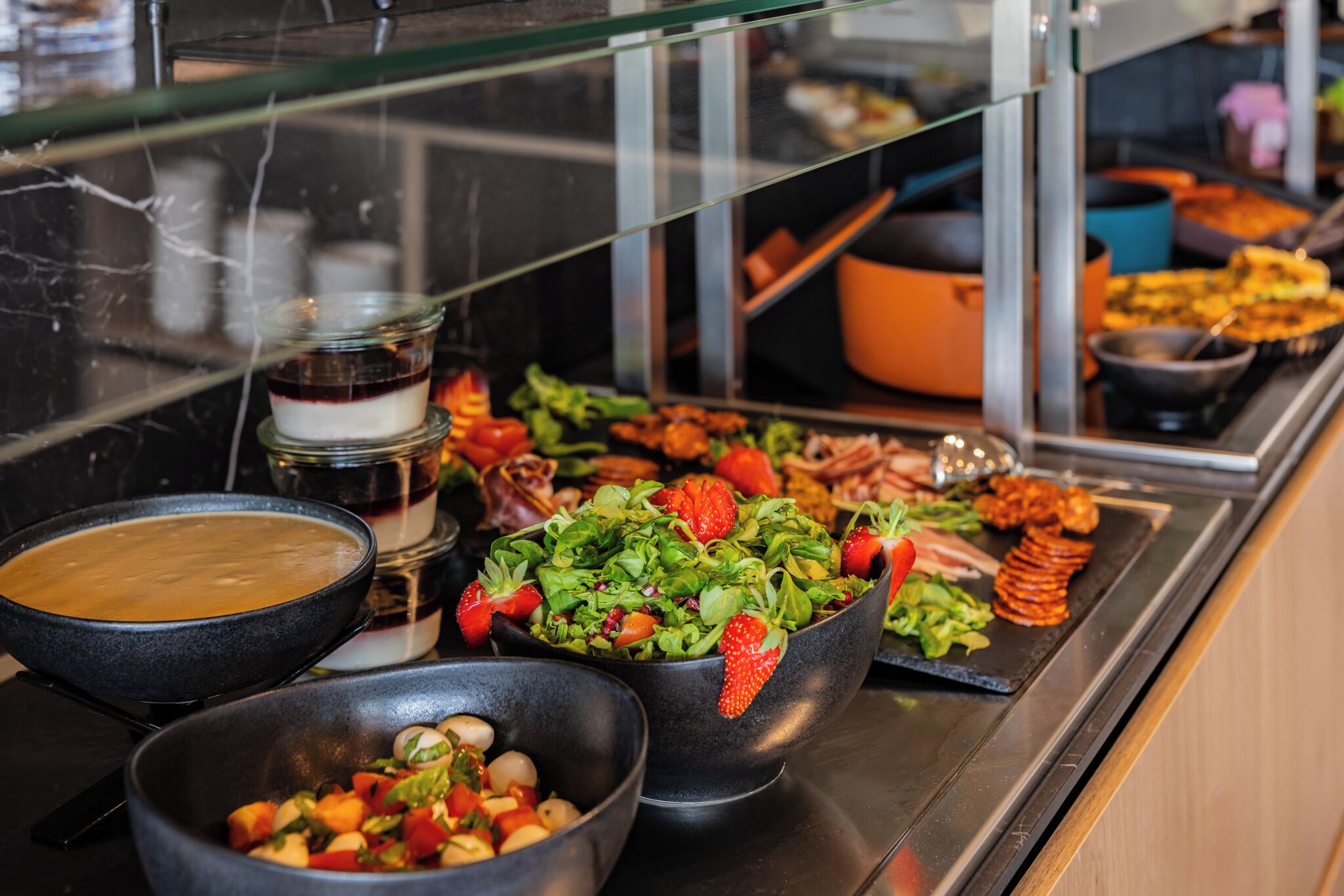 A buffet with various dishes including a bowl of soup, a salad with strawberries, and sliced meats.