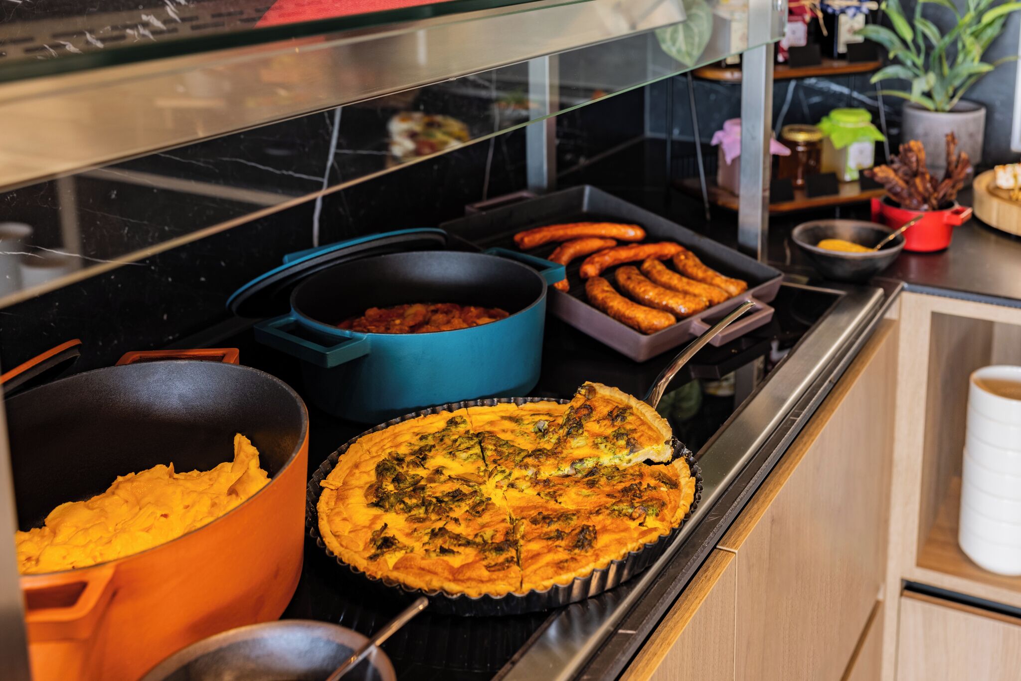 Un bufé con diversos platos, incluyendo una quiche, salchichas y un pastel.