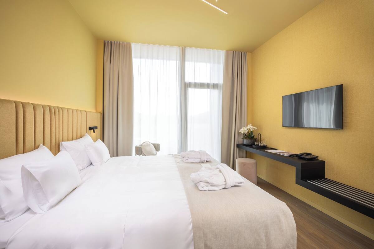 Una habitación de hotel con una cama grande, un escritorio con teléfono y un televisor montado.