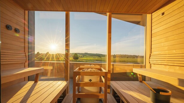 Eine Sauna mit Holzbänken und einer zentralen Heizung, mit Blick auf eine ländliche Landschaft.