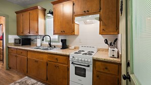 Cucina con pensili in legno, piano cottura bianco, forno a microonde e lavello.