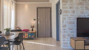 A living room with a TV, a dining area with a table and chairs, a door, and a stone wall. - Modern Greek Escape close to Alimos Shore (Alimos)