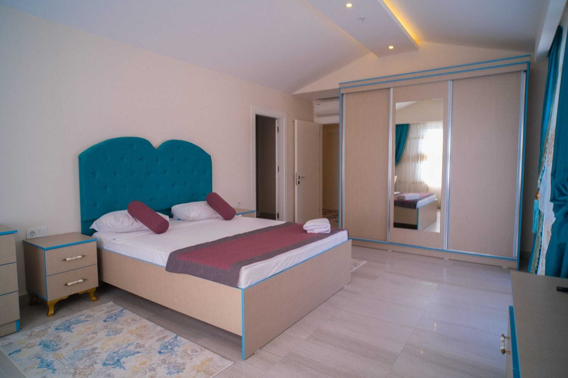 A bedroom with a large bed, a bedside table, a wardrobe, and a mirror.
