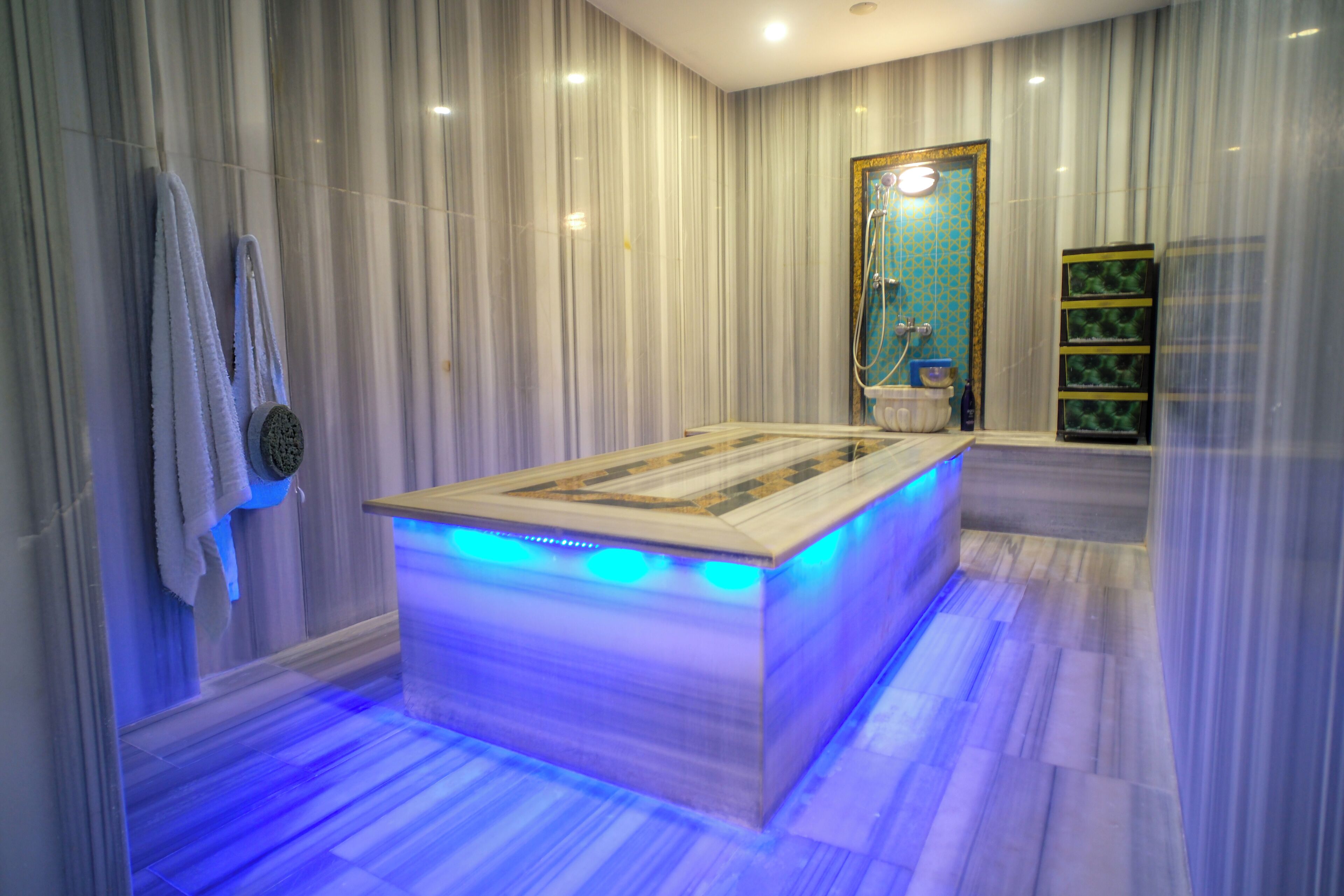 A modern bathroom with a large, illuminated bathtub, marble walls, and a wooden floor.