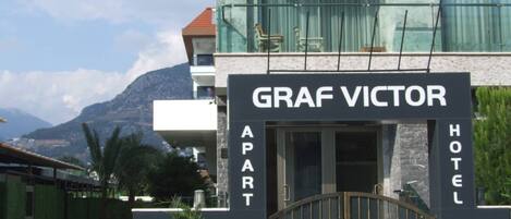 Entrada de un hotel con un letrero que dice "GRAF VICTOR APART HOTEL" y una entrada protegida por una reja.
