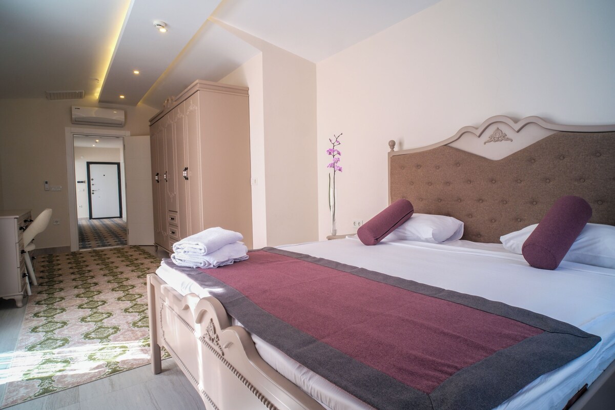A hotel room with a large bed, a wardrobe, a desk, and a chair.