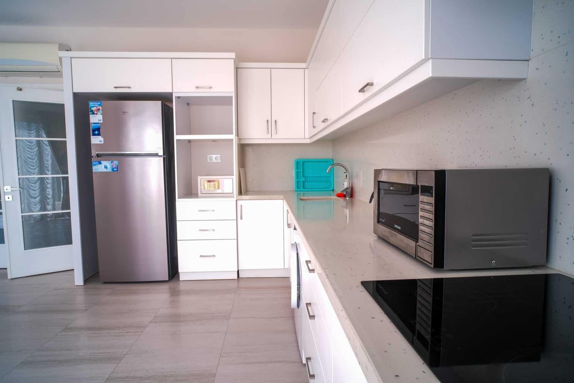 A modern kitchen with white cabinets, a stainless steel refrigerator, a microwave, and a black oven.