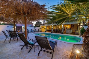 A poolside area with lounge chairs, a stone patio, and a building with a bar and pool. - Villa Andrea Zadarvillas (Nin)