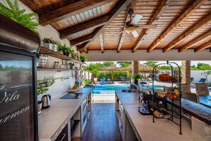 A kitchen with a view of a pool, wooden ceiling beams, and various kitchen appliances. - Villa Andrea Zadarvillas (Nin)