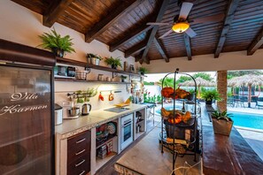A kitchen with a built-in refrigerator, shelves with plants, and a view of a pool area. - Villa Andrea Zadarvillas (Nin)