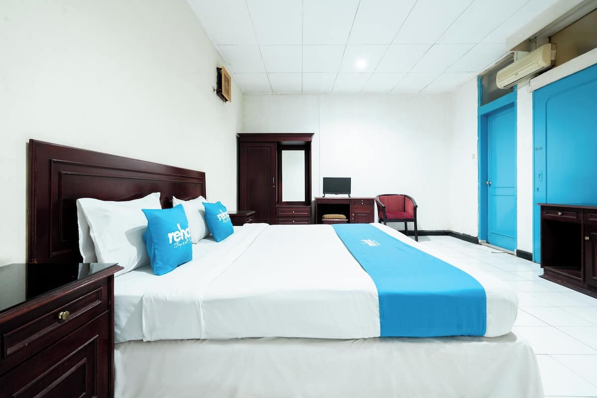 A hotel room with a large bed, a desk, a chair, and a wardrobe.