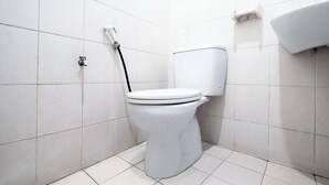A white toilet with a bidet attachment in a bathroom with white tiled walls and floor. - Sartika Hotel (Bandung)