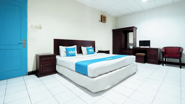 A hotel room with a large bed, a desk, a chair, and a wardrobe. - Sartika Hotel (Bandung)