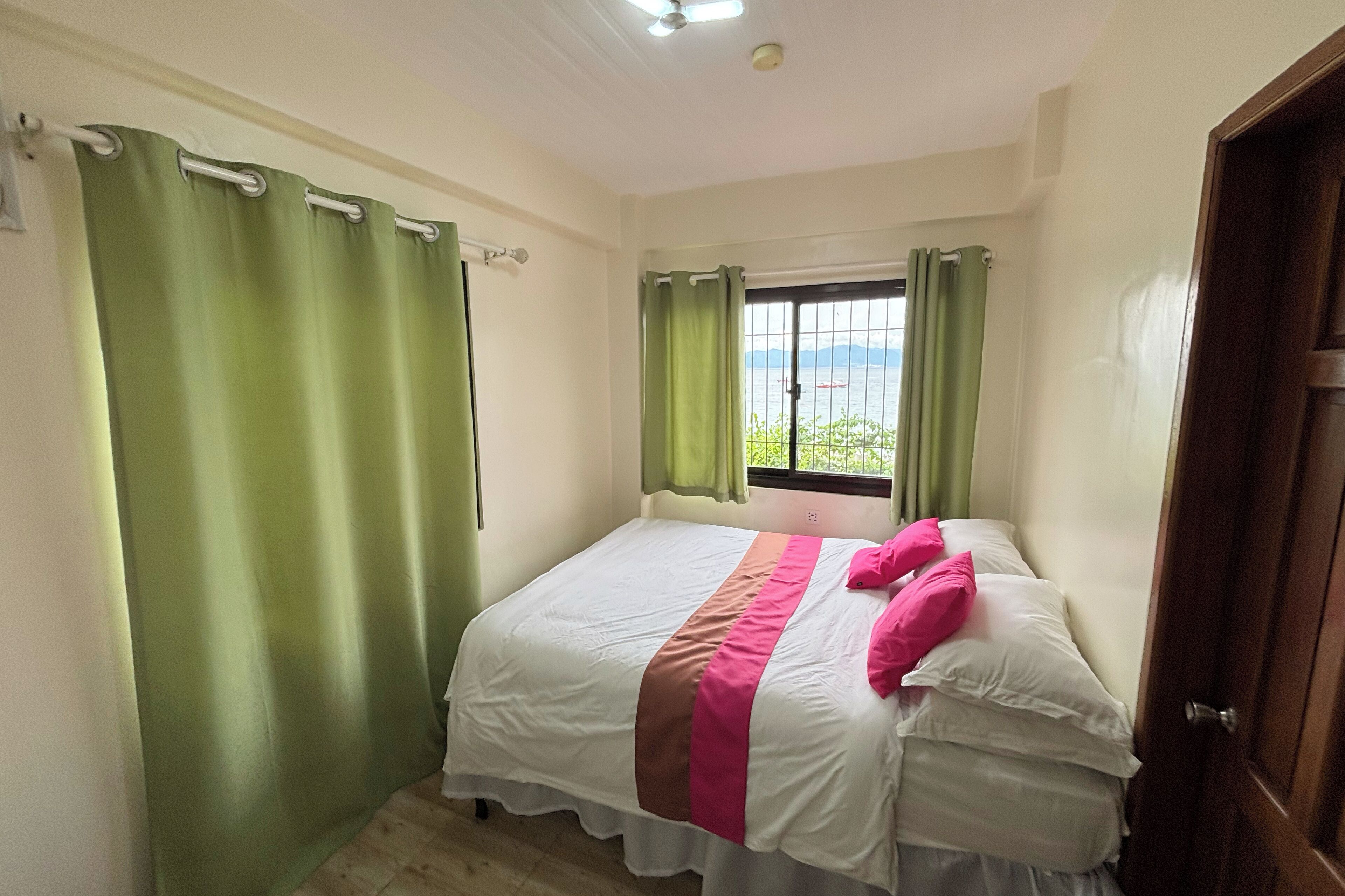 A bedroom with a bed, green curtains, a window with a view, and a door.