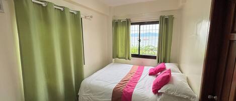A bedroom with a bed, green curtains, a window with a view, and a door.