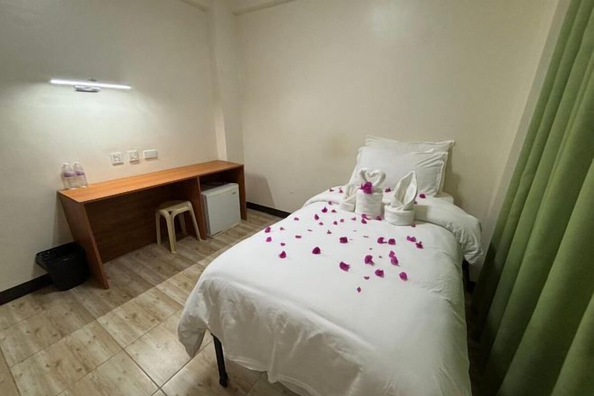 A hotel room with a bed, a desk, a chair, and a small stool.