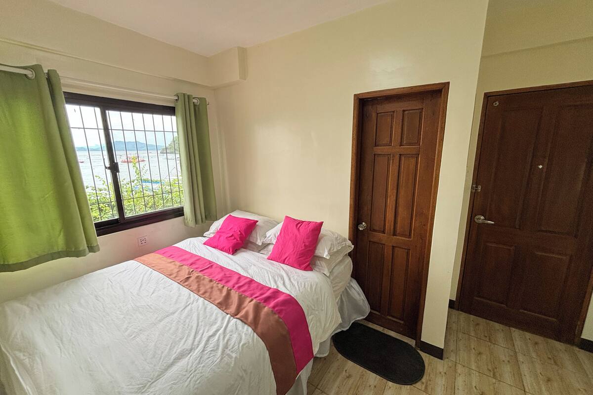 Un dormitorio con cama, ventana con cortinas y una puerta.