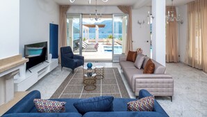 A living room with a sofa, armchair, TV, and a view of a pool and mountains. - 4-bedroom villa in wonderful Strp, Kotor with WiFi, fitness room (Strp, Kotor)