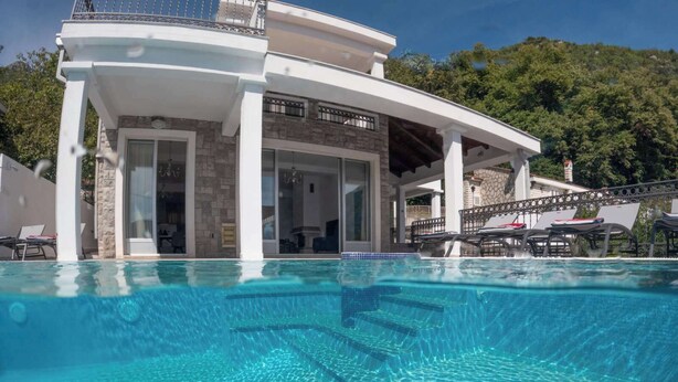 A modern poolside area with clear blue water, a covered seating area, and a stone building with large windows. - 4-bedroom villa in wonderful Strp, Kotor with WiFi, fitness room (Strp, Kotor)