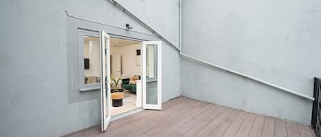 An open wooden deck with a sliding glass door leading to a living room with a sofa and a coffee table.