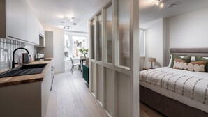 Une cuisine moderne avec un évier noir et un plan de travail en bois, un coin repas avec une table et des chaises, et une chambre avec un lit et des oreillers.