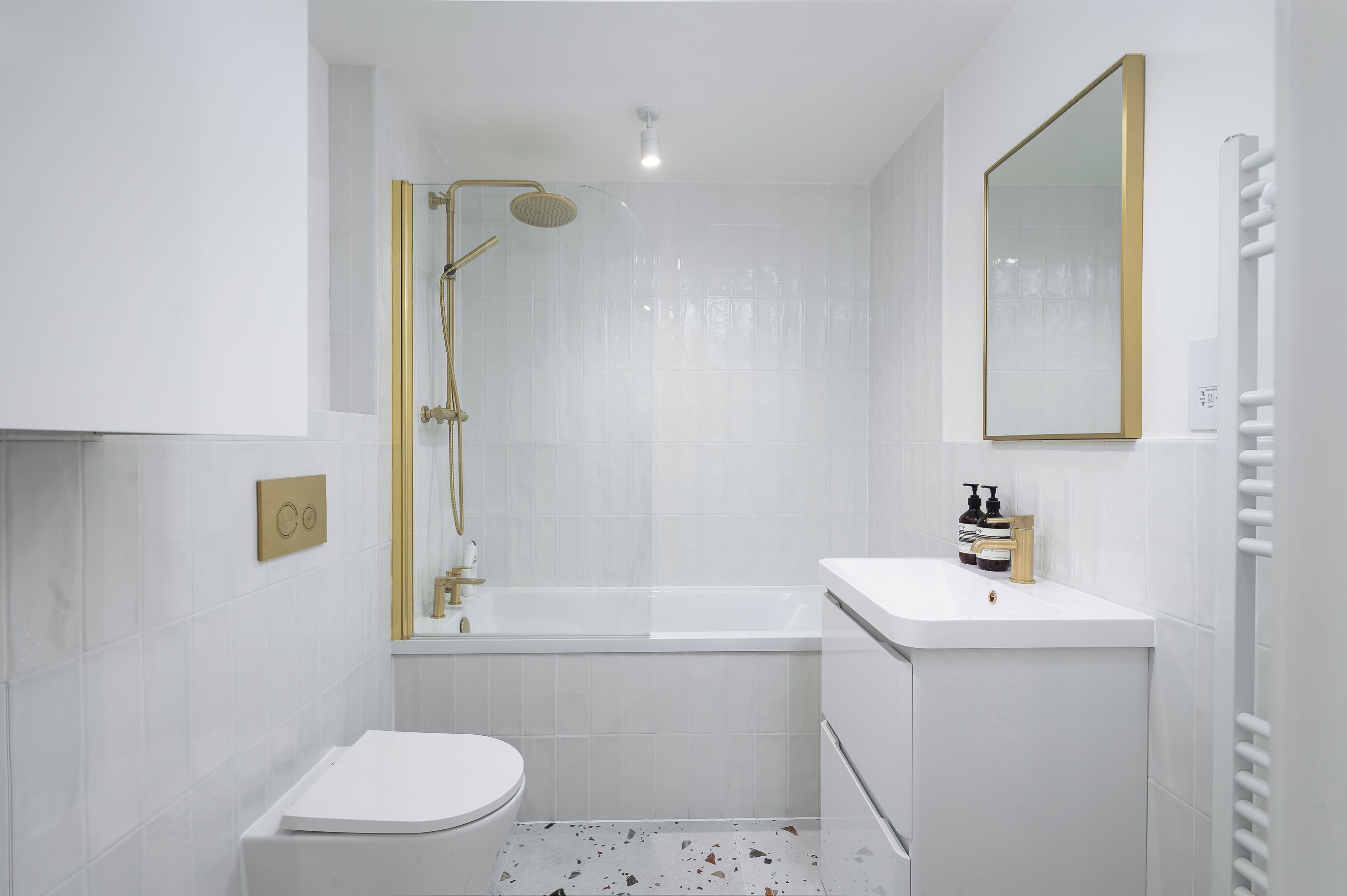A modern bathroom with a white toilet, a bathtub, and a shower with a gold frame.