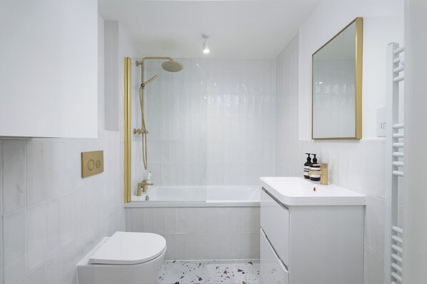 A modern bathroom with a white toilet, a bathtub, and a shower with a gold frame. - VESTO Brighton (Brighton)