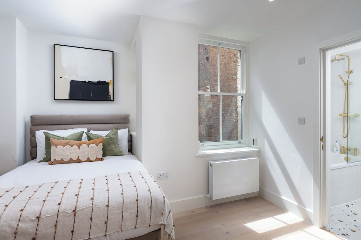 A bedroom with a bed, a window, a radiator, and a shower area.