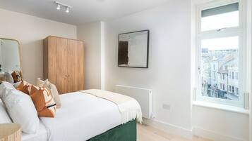 Un dormitorio con cama, armario de madera, espejo, radiador y ventana con vista a la ciudad.