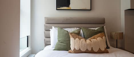 A neatly made bed with a headboard, a window with blinds, and a wall-mounted abstract painting.