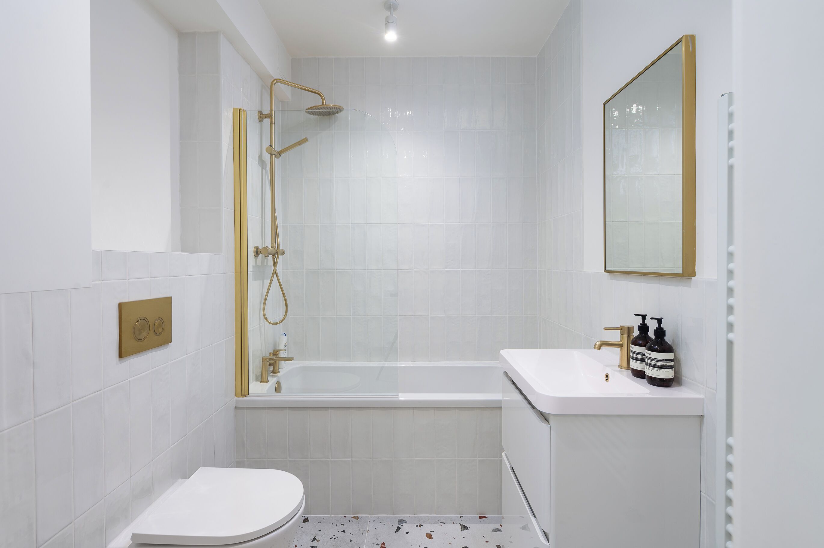 A modern bathroom with a white bathtub, a toilet, and a sink with two bottles of soap.