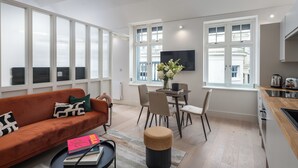 Un salon moderne comprenant un canapé, une table à manger, des chaises et un coin cuisine avec une télévision et une fenêtre.