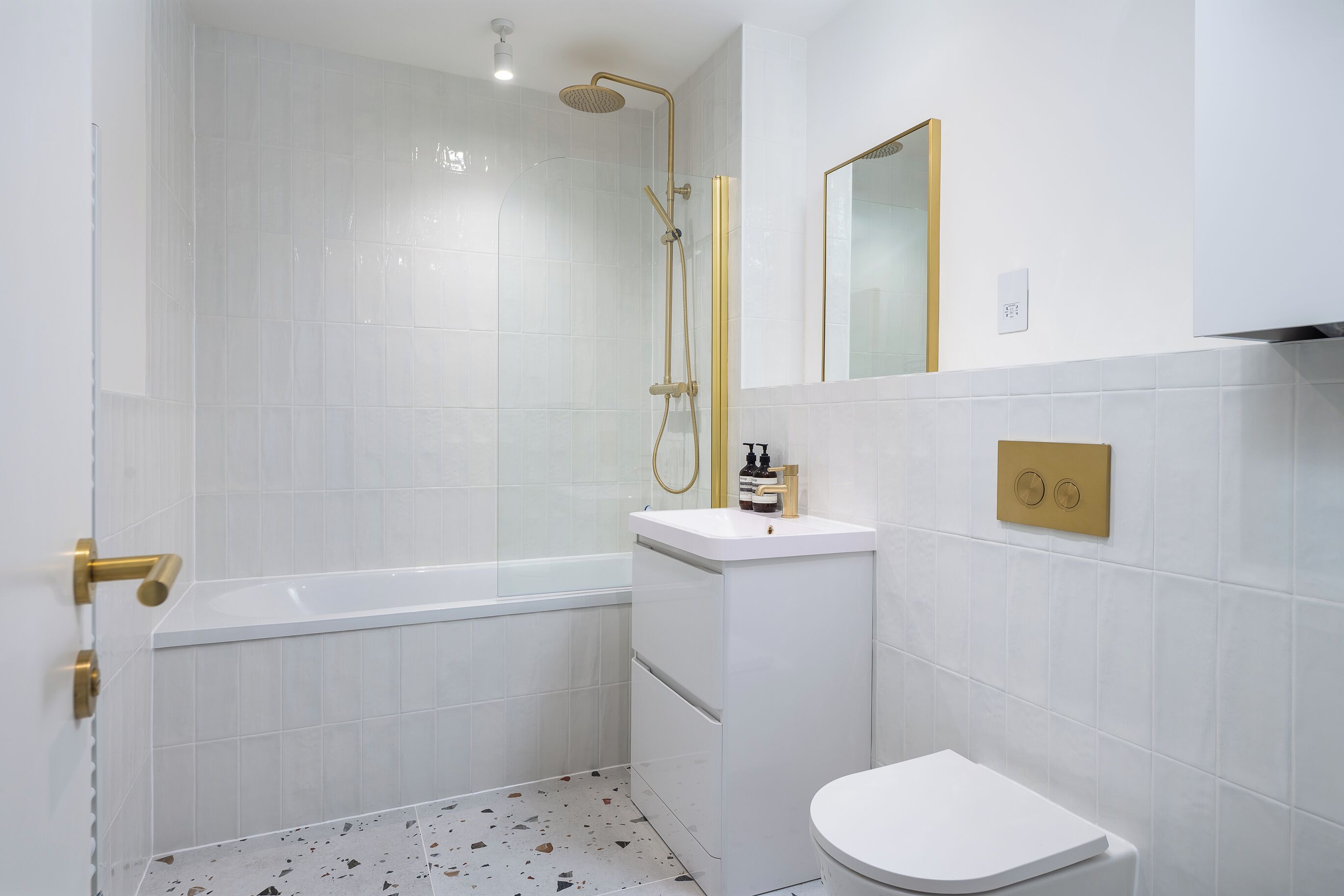 Et badeværelse med badekar, toilet, vask og bruser med gylden brusehoved.