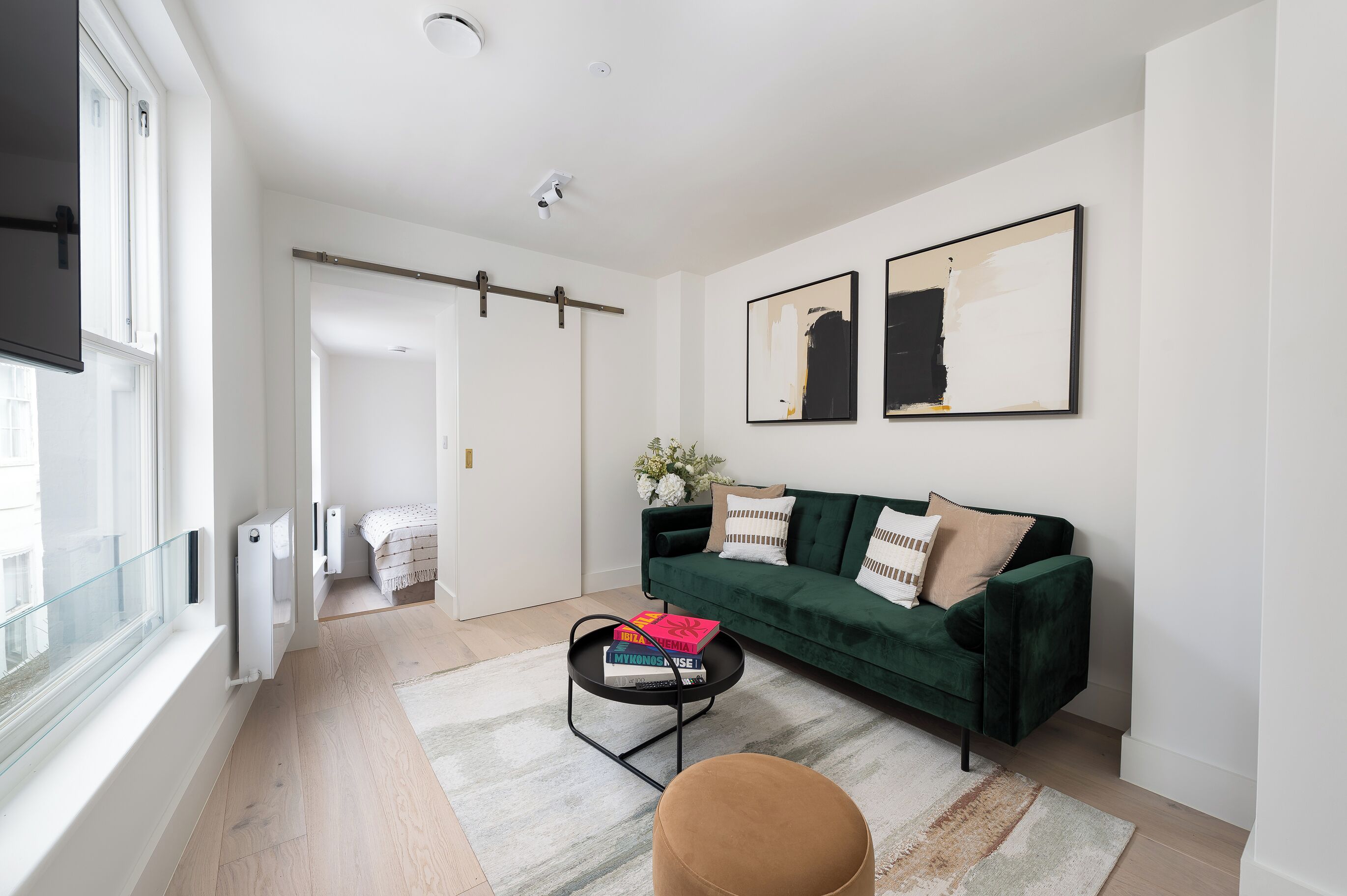 En moderne stue med en grøn sofa, et sofabord med bøger og et stort vindue.
