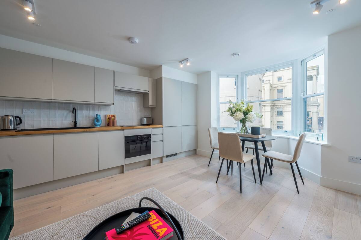 A modern kitchen with white cabinets, a wooden countertop, and a dining area with a table and chairs.