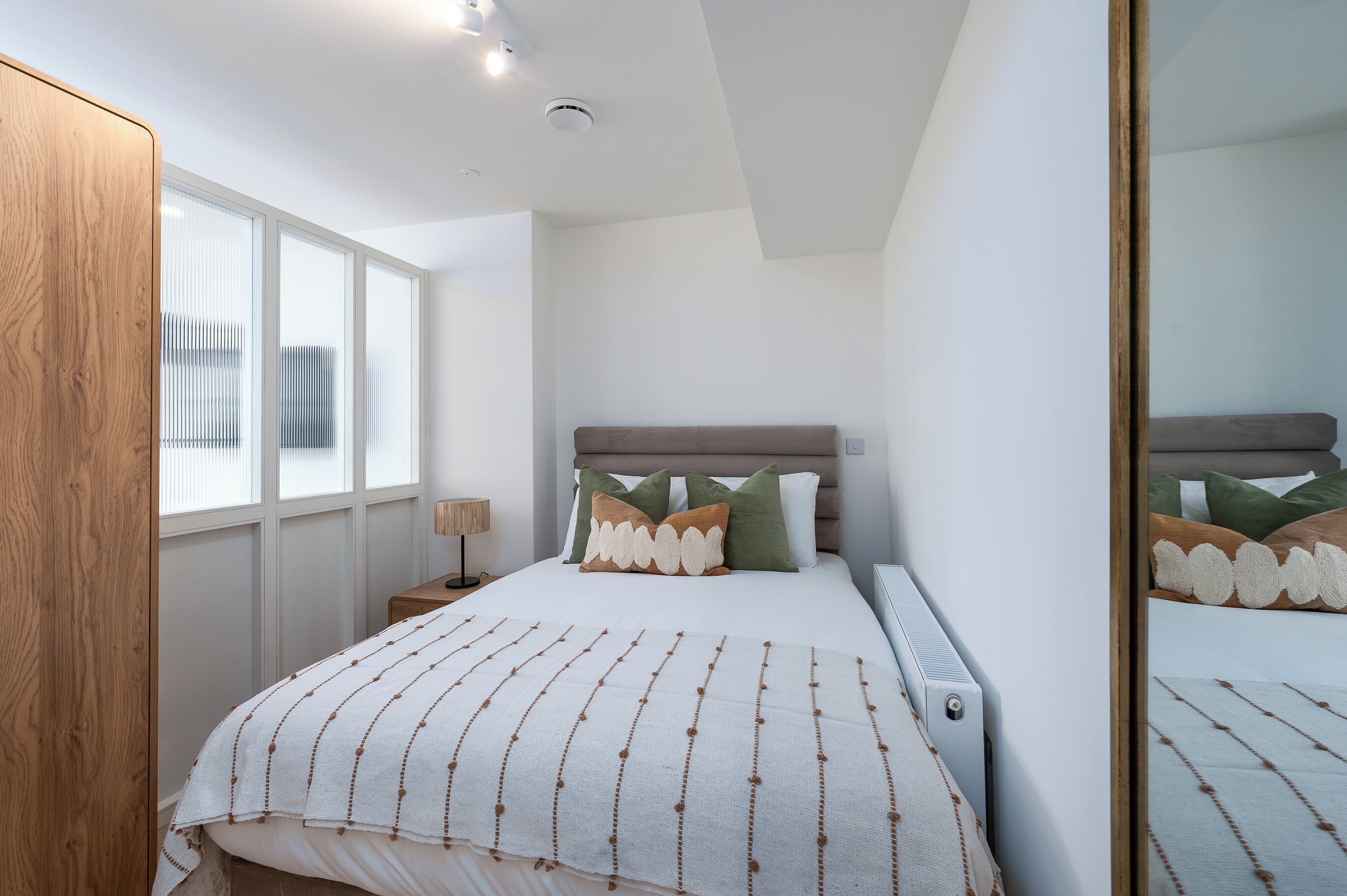 A bedroom with a bed, a nightstand, a window, and a mirror.