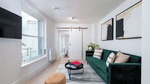 A modern living room with a green sofa, a coffee table with books, and a large window. - VESTO Brighton (Brighton)