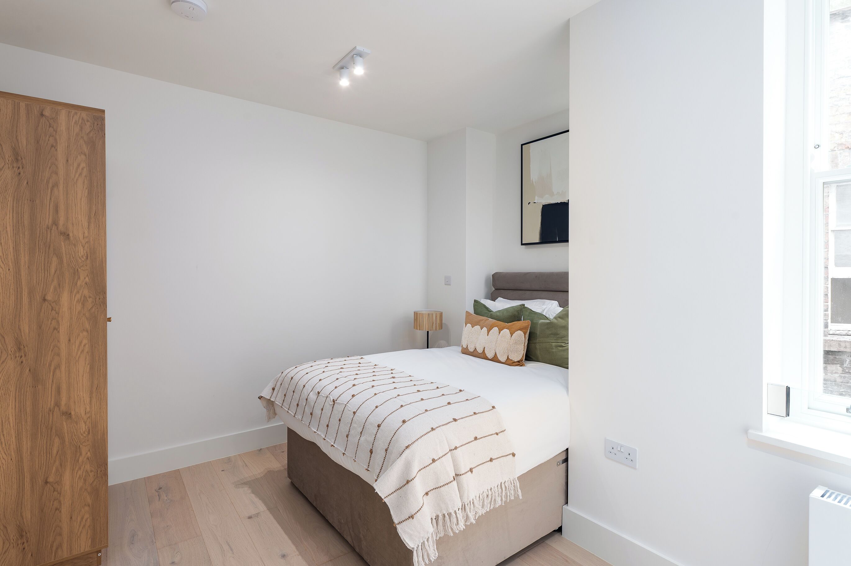 Un dormitorio con cama, armario de madera, lámpara de noche y ventana.