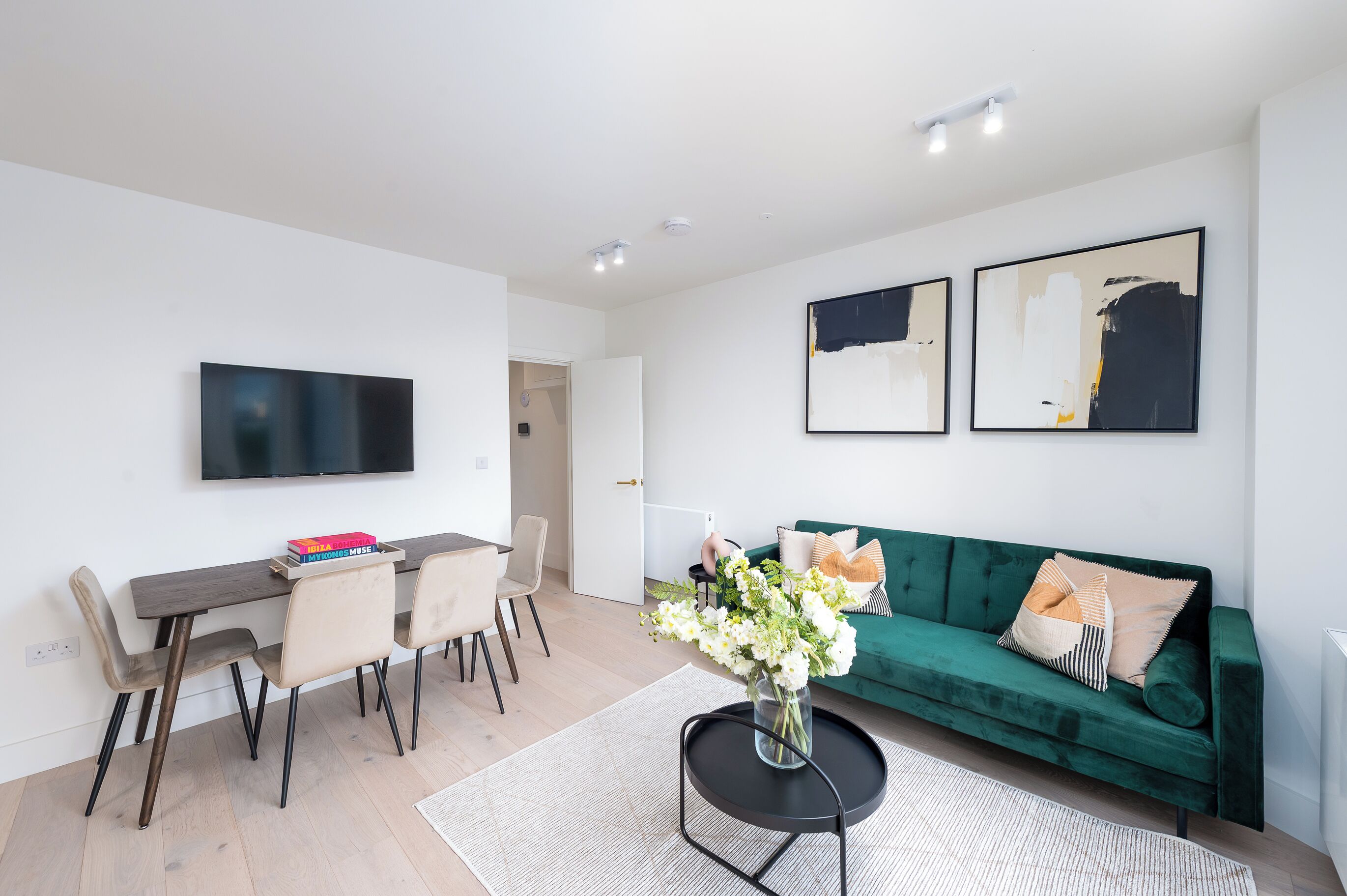 Ein modernes Wohnzimmer mit Essbereich, einem grünen Sofa und zwei abstrakten Bildern an der Wand.