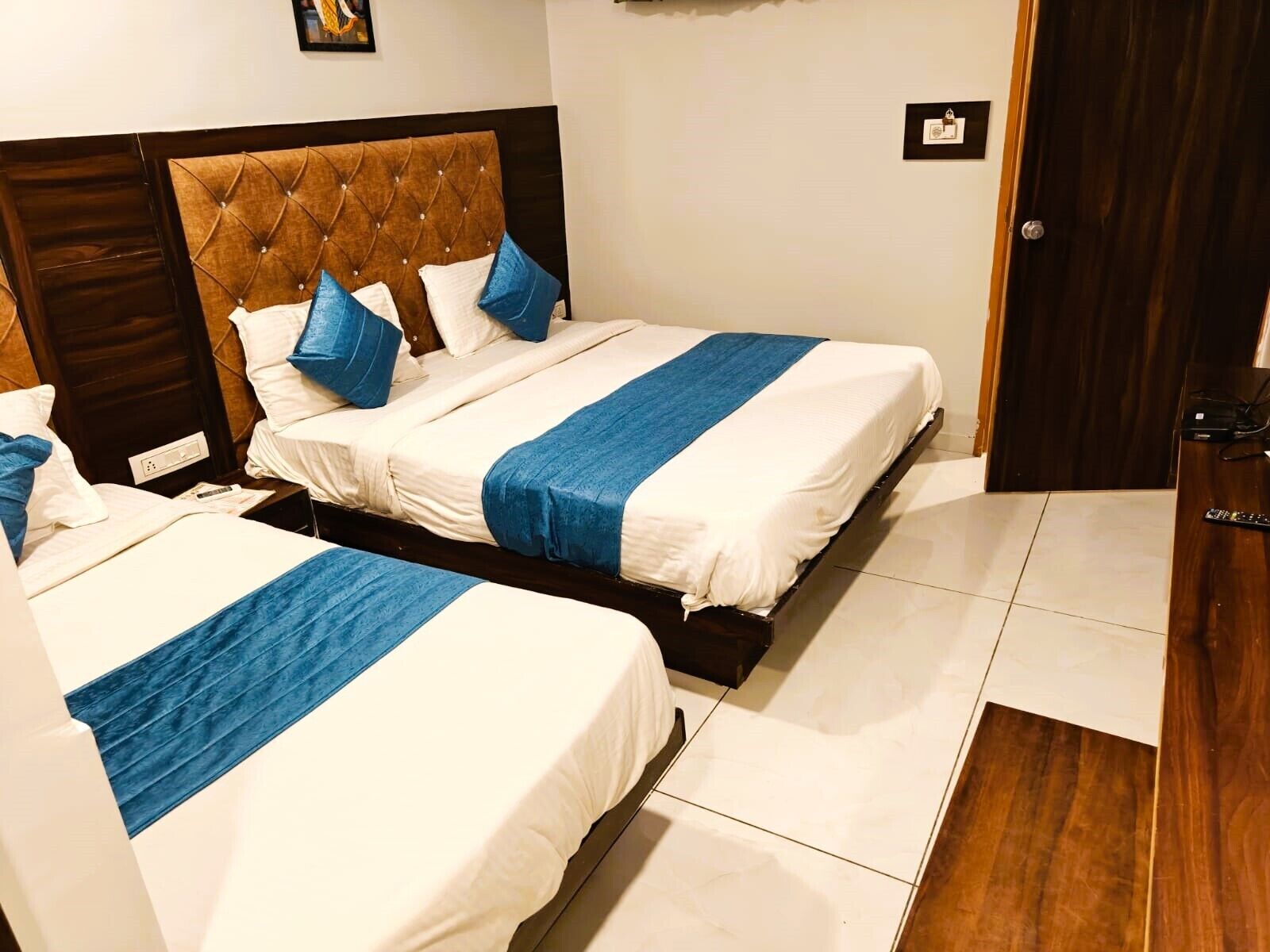 Quarto de hotel com duas camas, uma cabeceira de madeira e um edredom azul listrado.
