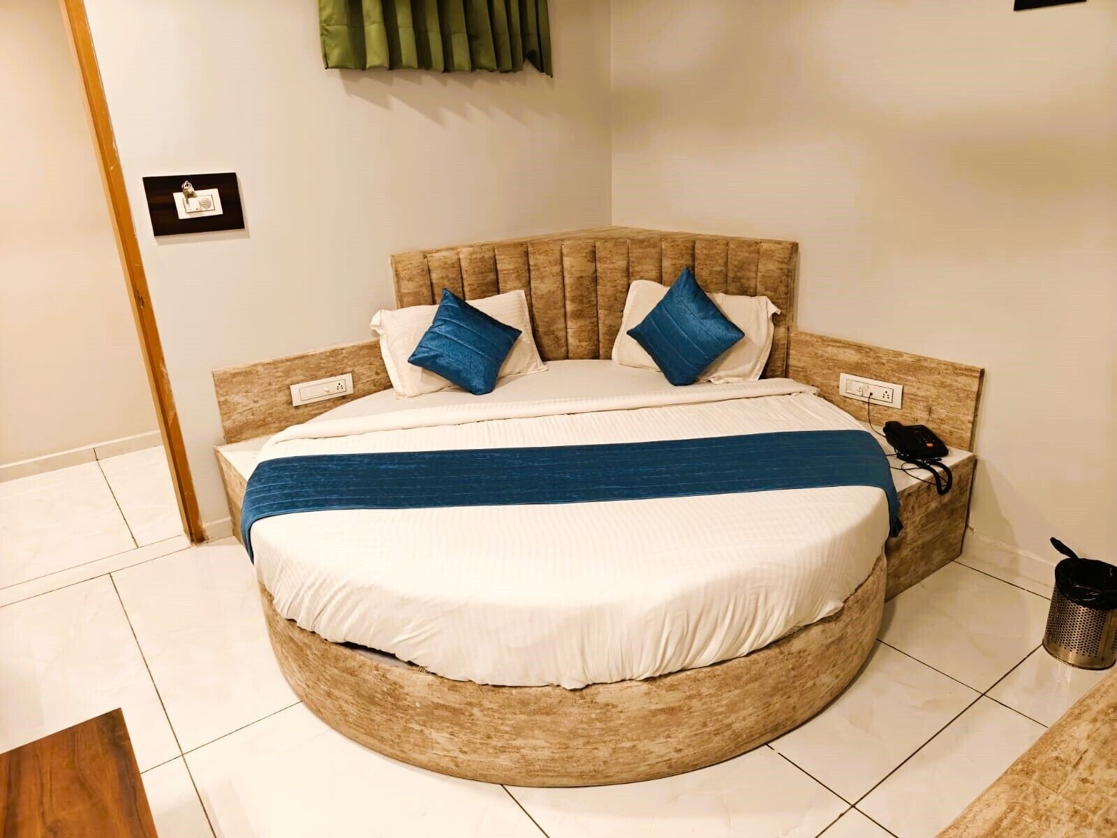 Ein rundes Bett mit Holz-Kopfteil, zwei Kissen, einer blauen Decke und einem Telefon daneben.