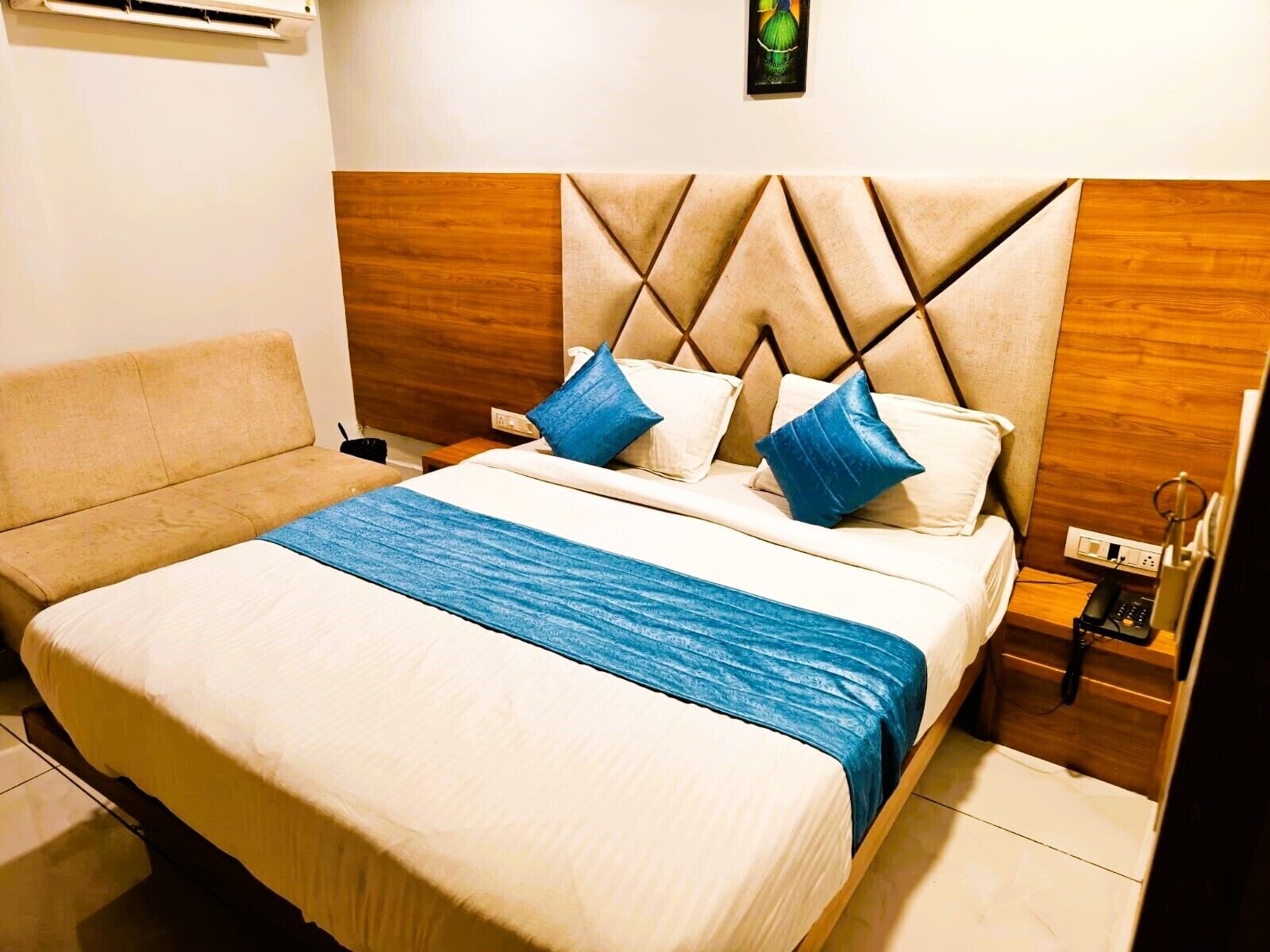A hotel room with a bed, a bedside table, a lamp, and a wall-mounted air conditioner.