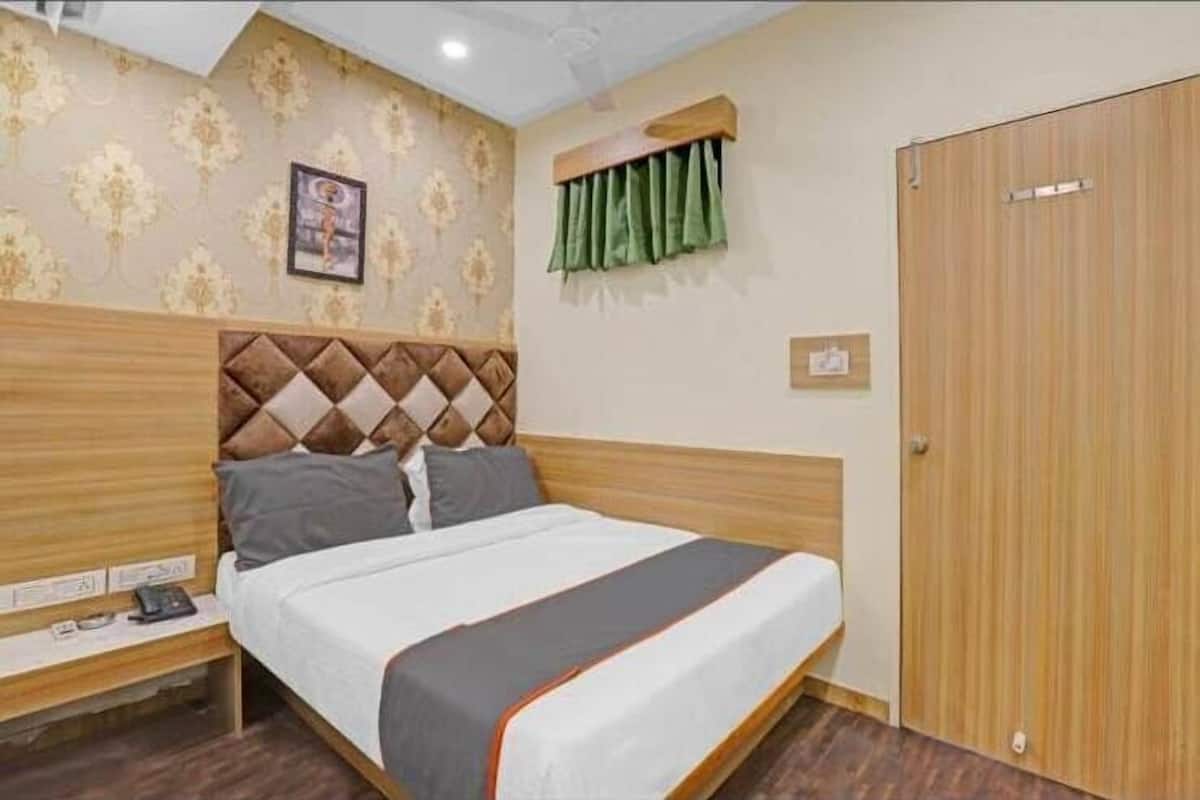 A neatly arranged hotel room with a bed, a nightstand, a wooden wardrobe, and a patterned wall.