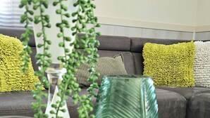 Un salon avec un canapé, des coussins, une plante verte, des bougies et un objet décoratif posé sur une table.