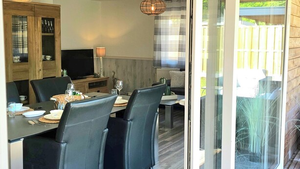 Un coin repas avec une table dressée pour quatre personnes, un téléviseur et un meuble en bois doté de portes en verre.