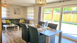 Un salon moderne avec un canapé, une table à manger pour quatre personnes et une grande fenêtre donnant sur une clôture en bois.