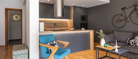 Un espacio moderno para estar con una isla de cocina, un sillón azul, un sofá y una bicicleta colgada en la pared.