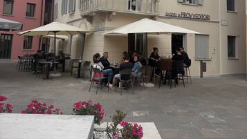 An outdoor café area with tables and chairs, a building with a balcony, and a sign that reads 'Locanda ai PROV EDITORI'.