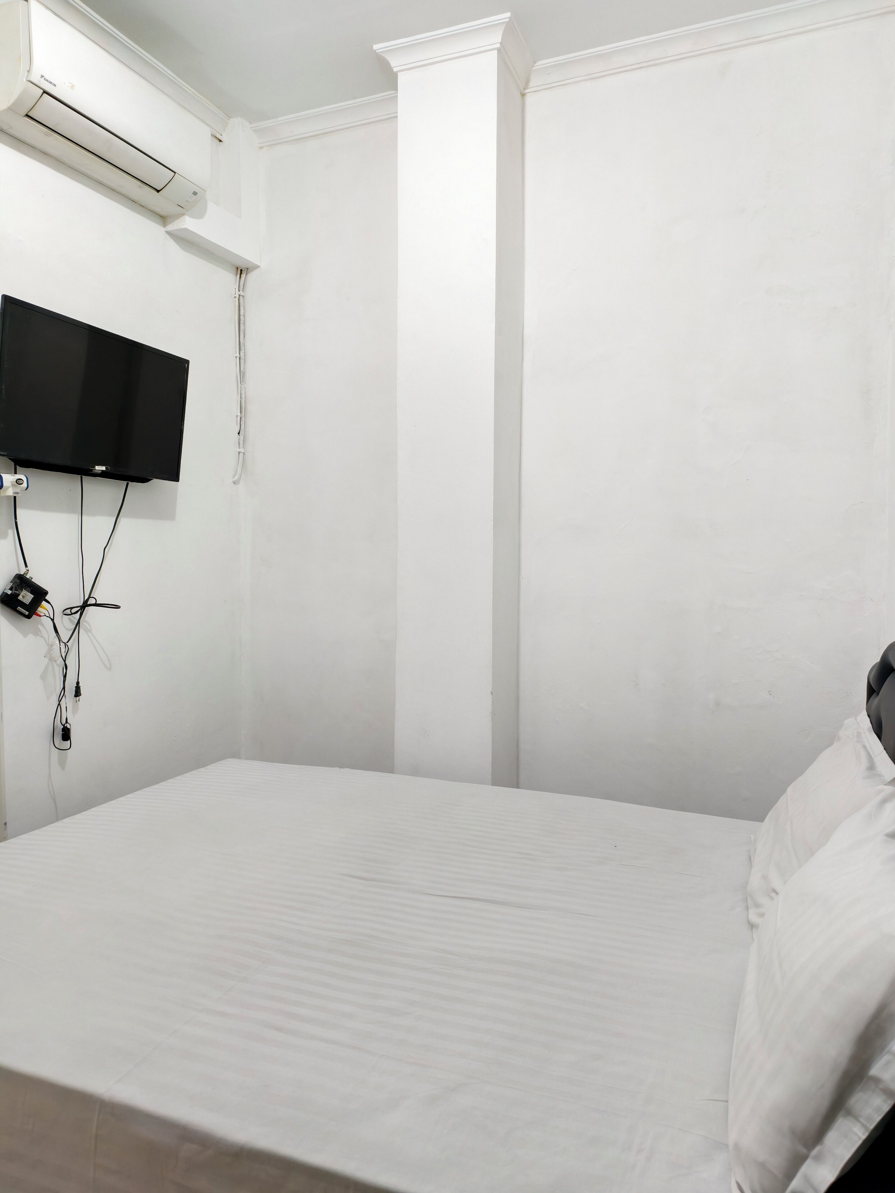 A room with a bed, a mounted TV, and an air conditioning unit.